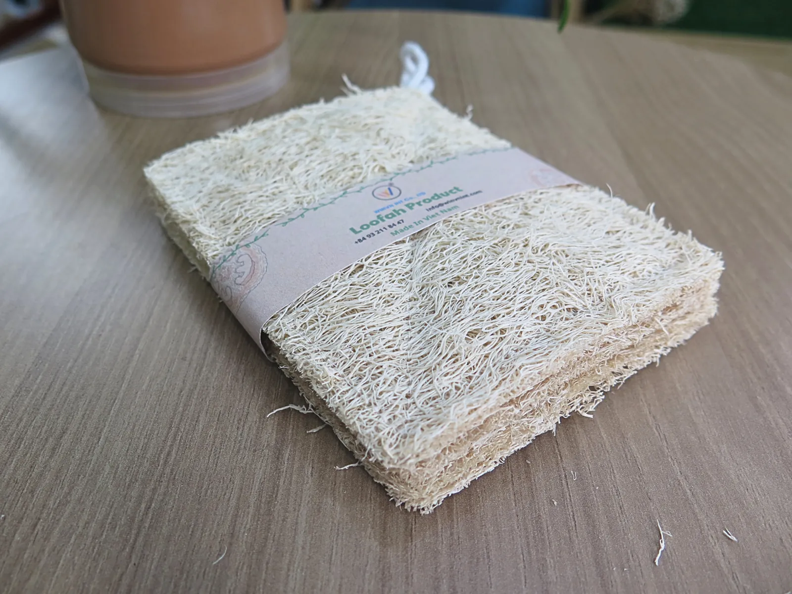 Stack of natural loofah dish pads held with a kraft paper band on a wooden surface