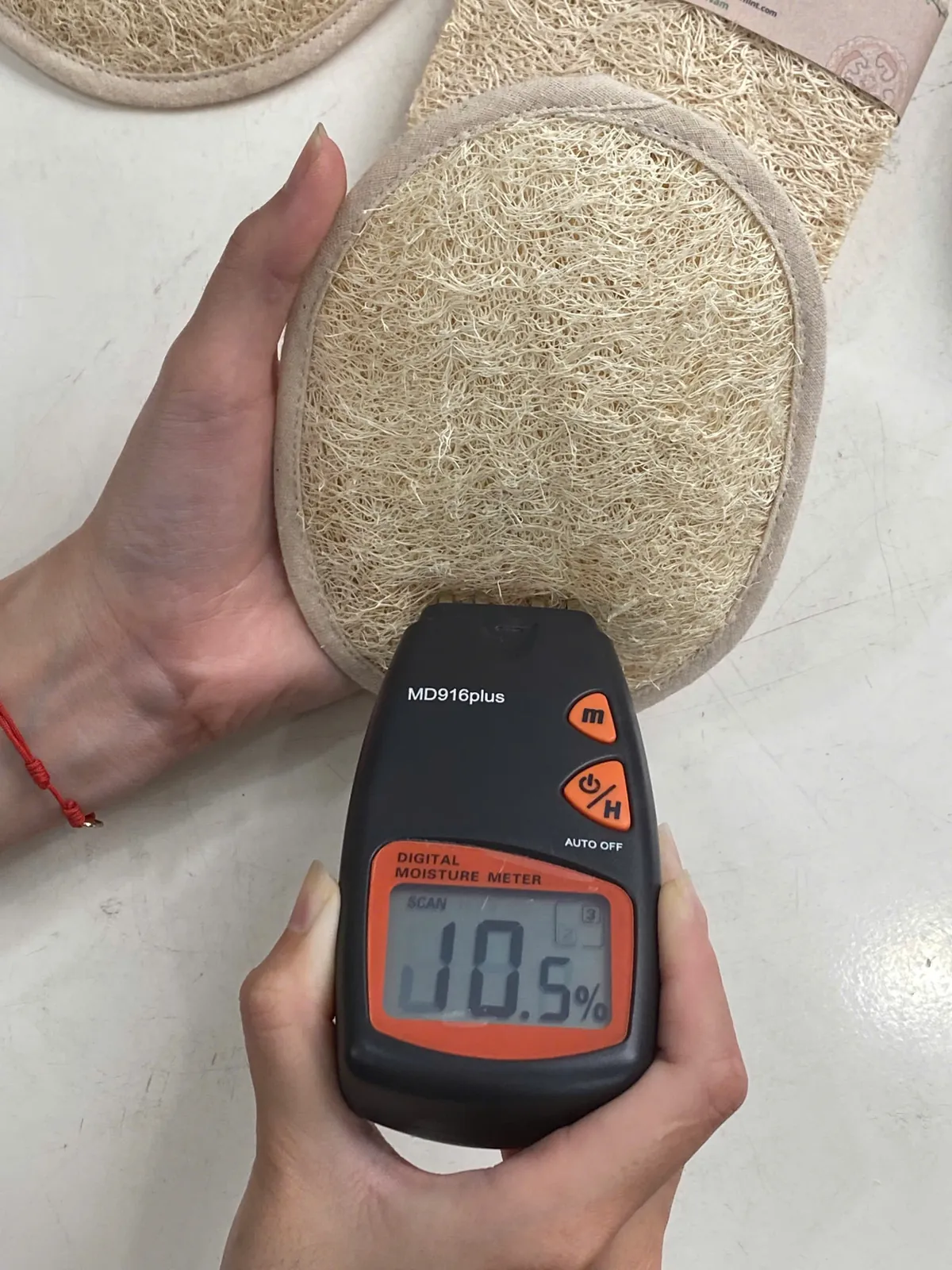 Digital moisture meter reading 10.5% on an oval natural loofah exfoliating pad