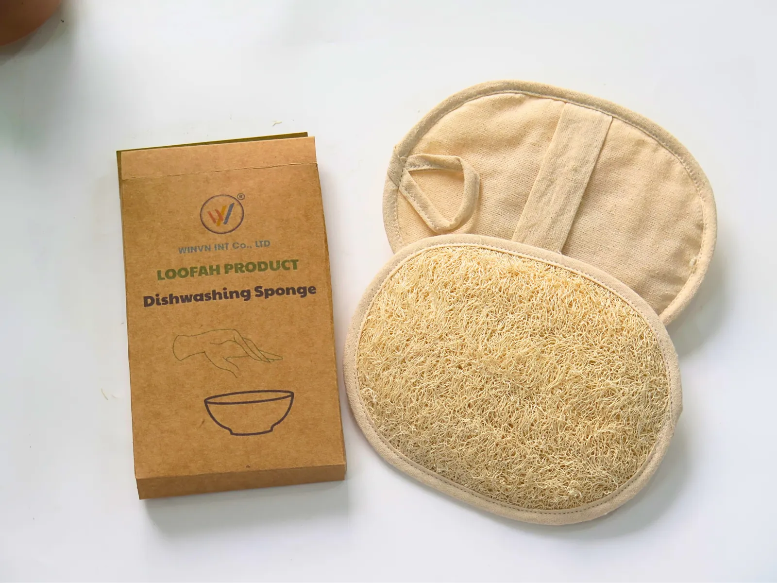 Oval loofah exfoliating pad with fabric back next to a kraft retail box
